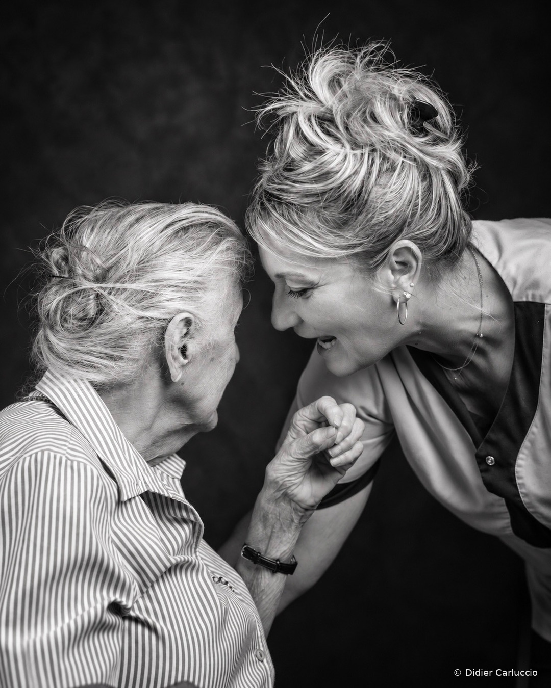 L’art d’écouter Photographie de Didier Carluccio illustrant un moment de complicité entre une résidente âgée et une soignante lors d'une séance de portraits en EHPAD. La soignante accompagne et rassure la résidente, créant un instant de confiance et de bienveillance.